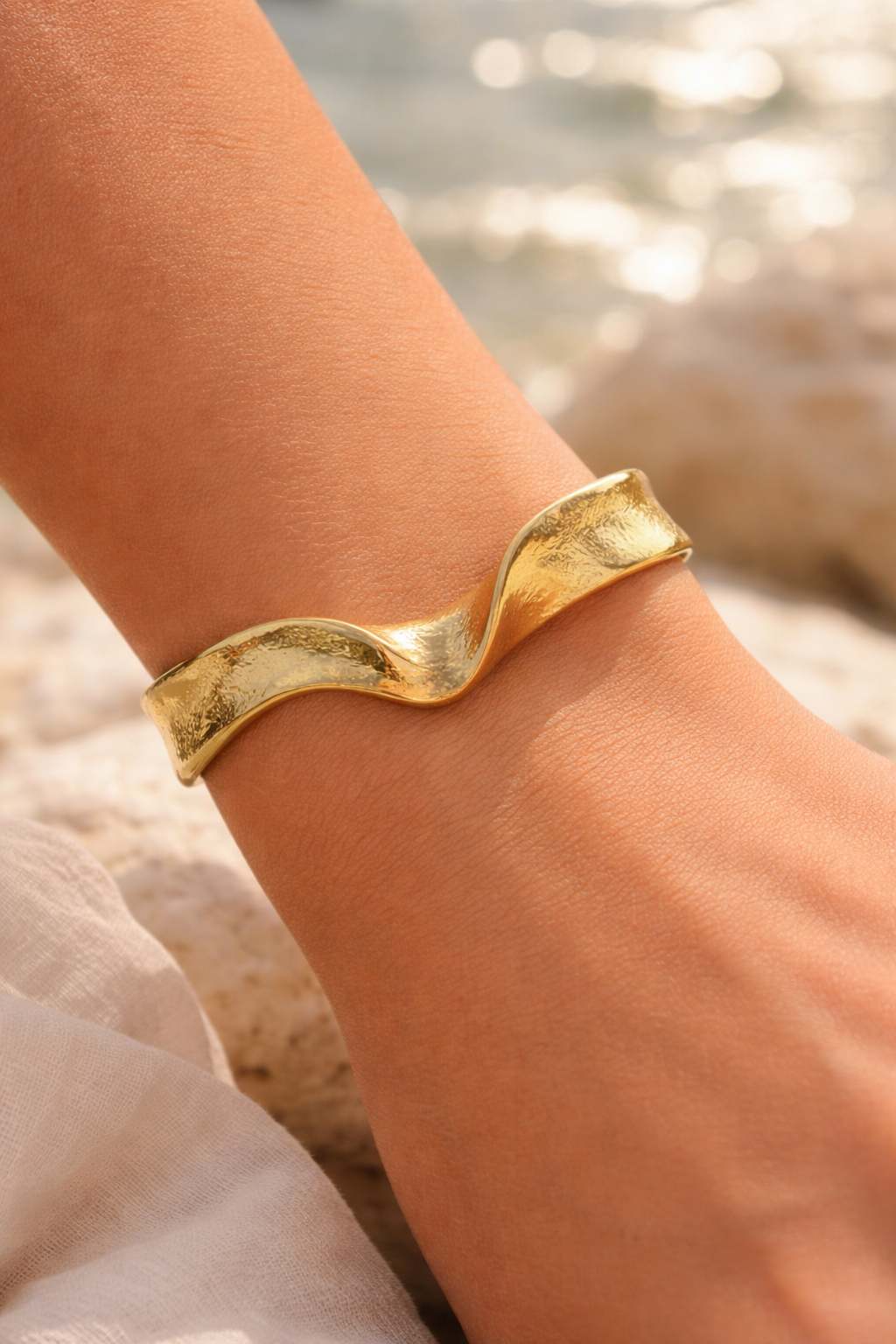 Bracelet manchette or torsadé, porté au poignet, plage