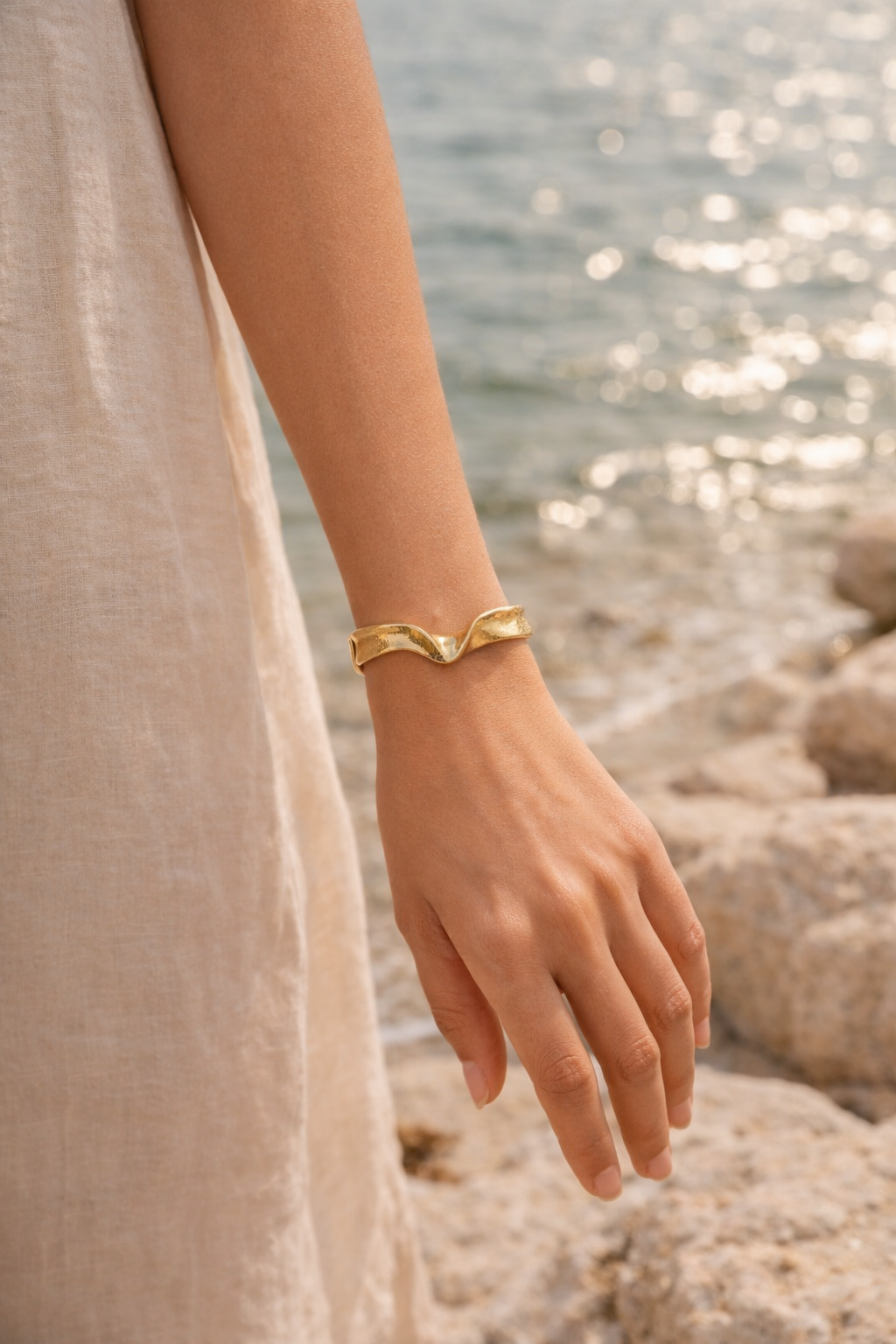 Bracelet manchette or vague, porté au poignet, plage